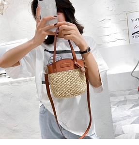Detail of straw bucket bag featuring dark brown leather patchwork and a brand logo label