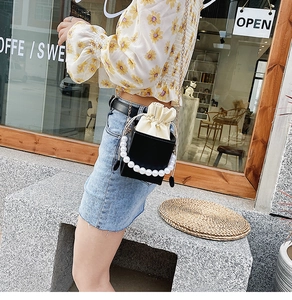 Close-up of black crossbody bag with pearl handle and beige drawstring pouch