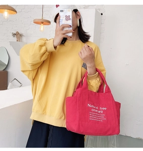 Detail view of a red canvas tote bag with white artistic typography and hand straps