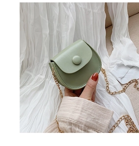 Detail of a mini bean green crossbody bag with gold chain strap held in hand