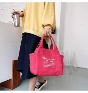 Detail of red canvas tote bag with side pocket and white printed decorative text