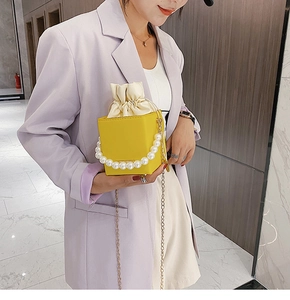 Detailed shot of yellow crossbody bag with pearl handle and golden chain on purple blazer