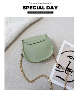 Flat lay of a mint green mini saddle bag with golden chain strap on a textured surface