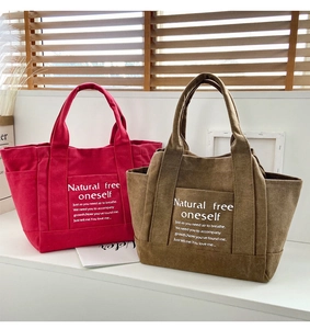 Close-up of canvas tote bags in red and brown with side pockets and inspirational text