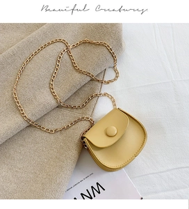 Close-up of cream yellow leather mini crossbody bag with gold chain strap on beige fabric