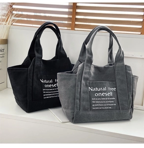 Close-up of black and grey canvas tote bags with side pockets and printed slogans
