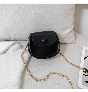 Detail shot of black faux leather mini saddle bag with golden chain on soft knit fabric