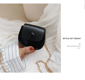 Detail of mini black textured leather round bag with gold chain strap and buckle