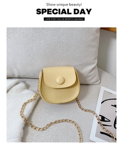Close-up of yellow faux leather saddle bag with round buckle and golden chain strap