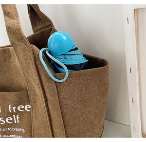 Detail of brown canvas tote side pocket holding a blue umbrella for storage