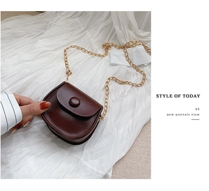 Detail of vintage brown leather mini crossbody bag with golden chain on white fabric