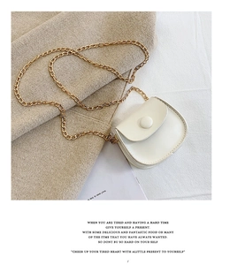 Detail view of a white mini round bag with gold chain strap on soft texture