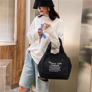 Large black canvas tote bag with white text print shown in a casual lifestyle street scene