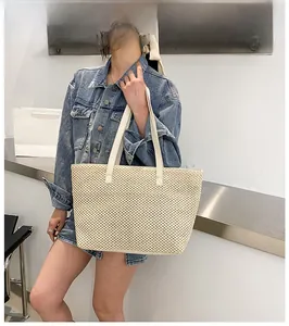 Model showcasing large beige woven tote bag with slim shoulder straps in minimalist setting