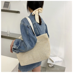 Detailed view of woven straw tote bag with white leather straps in a minimalist setting