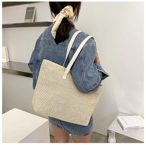 Detail view of woven beige tote bag texture with slim leather straps on a model