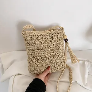Detail van handgeweven beige strooien tas met opengewerkte patronen en kralenkwastjes