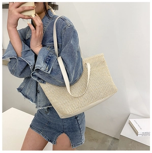 Detail of beige woven tote bag with white leather straps on a blue denim outfit