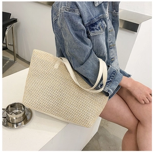 Close-up of beige woven linen tote bag with white leather straps in a cafe setting