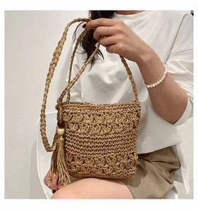 Detail of hand-woven straw crossbody bag featuring floral patterns and wood bead tassels