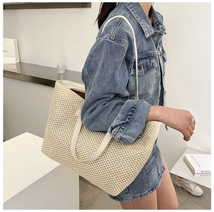 Detail of a large woven tote bag with white leather straps worn by a model in a minimal setting