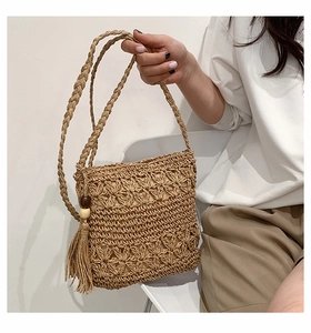 Detail of woven straw bag with floral cutouts, tassel charm and wooden beads on the side