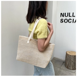 Detail of woven straw tote bag with white faux leather handles on a minimal background