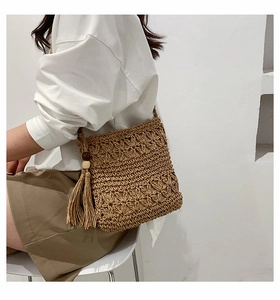 Detail of hand-woven straw crossbody bag with floral cutouts and wooden bead tassels
