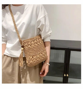 Detail of woven straw crossbody bag with intricate hollow patterns and long tassel charm