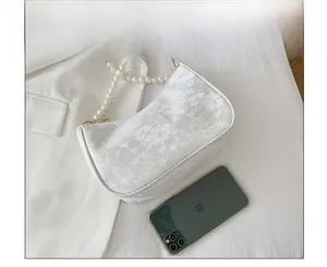 Close-up of elegant white lace shoulder bag with pearl strap next to a smartphone