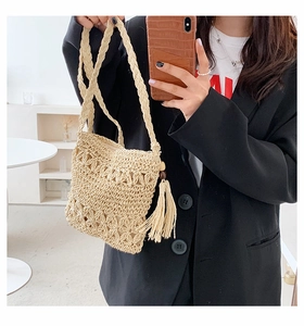 Detail of beige straw crossbody bag featuring woven texture and long tassel fringe