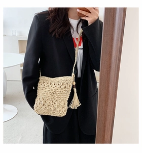 Detail of beige straw crossbody bag featuring intricate hollow out weave and long tassels