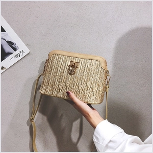 Detail van geweven strooien crossbodytas met metalen bijensluiting en leren riem