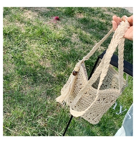Detail of beige woven straw bag featuring floral cutouts, fringe tassel, and zipper closure