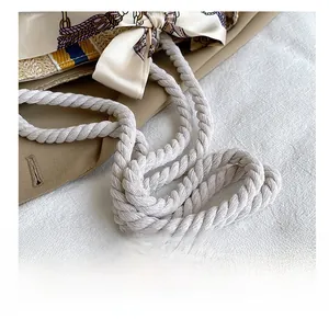 Detail of thick cotton rope shoulder strap and silk scarf on straw beach woven bag