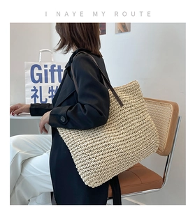 Detailed view of woven straw tote bag featuring brown leather shoulder straps on model