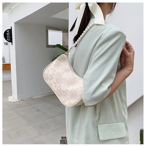 Detail of off-white lace shoulder bag with elegant pearl strap and gold hardware
