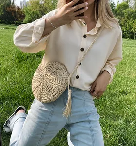 Detail van ronde strooien crossbodytas met kwastjes en zomerse outfit op het gras