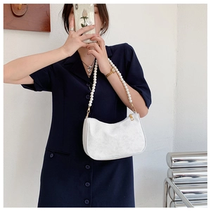 Detail of white embossed handbag with large pearl strap held by a model in blue dress