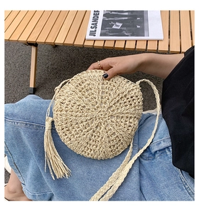 Close-up of beige woven straw round shoulder bag with tassel detail and braided strap