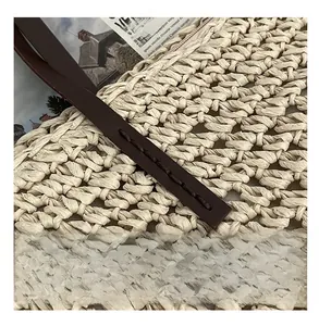 Close-up of precise stitching on leather handle and woven texture of straw beach bag