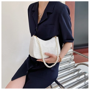 Detail of white embossed hobo bag featuring elegant large pearl handle and gold hardware