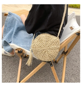 Close-up of a bohemian round woven straw bag with tassels and braided shoulder strap
