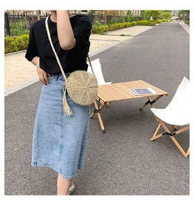 Detailed view of a round woven straw bag with boho fringes and a slim shoulder strap