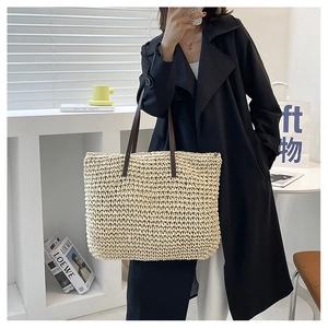Detail of handwoven straw tote bag featuring contrast dark brown leather shoulder straps
