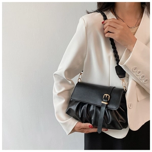 Close-up of black pleated shoulder bag with gold buckle and woven strap on a white blazer