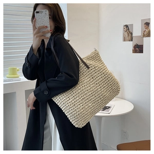 Close-up of woven straw tote bag with brown leather handles and secure metal zipper