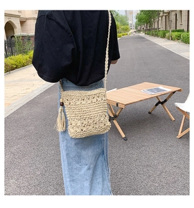 Detail of a beige woven straw crossbody bag with floral texture and long tassels