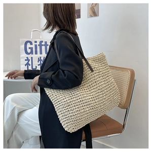 Detail of a large woven tote bag with brown leather straps shown on a model's shoulder