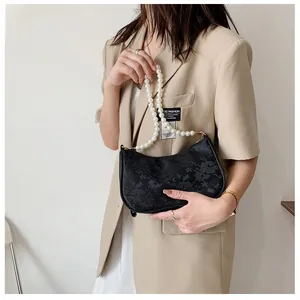 Close-up of black textured handbag with elegant pearl handle on a beige blazer background
